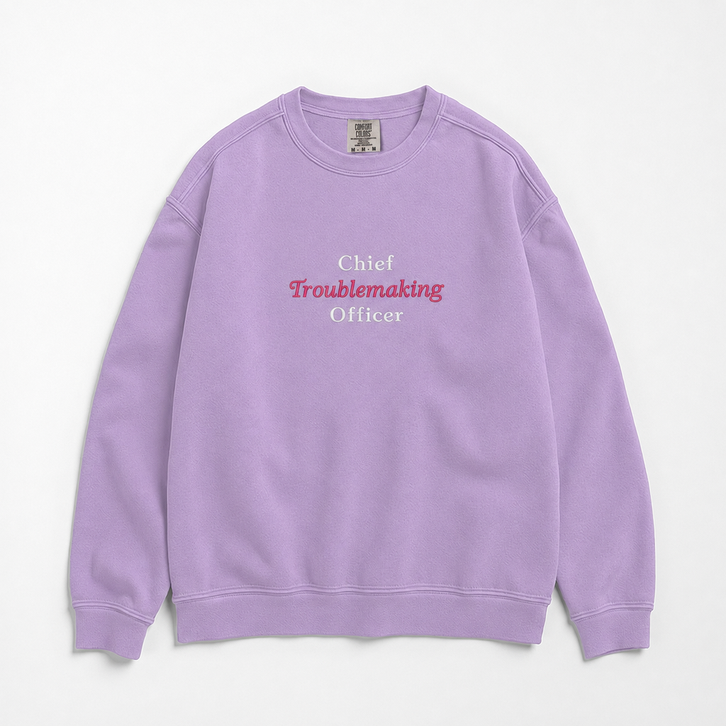 A light purple crewneck sweatshirt with the text 'Chief Troublemaking Officer' printed on the chest, featuring white and pink lettering, laid flat against a light off-white background.