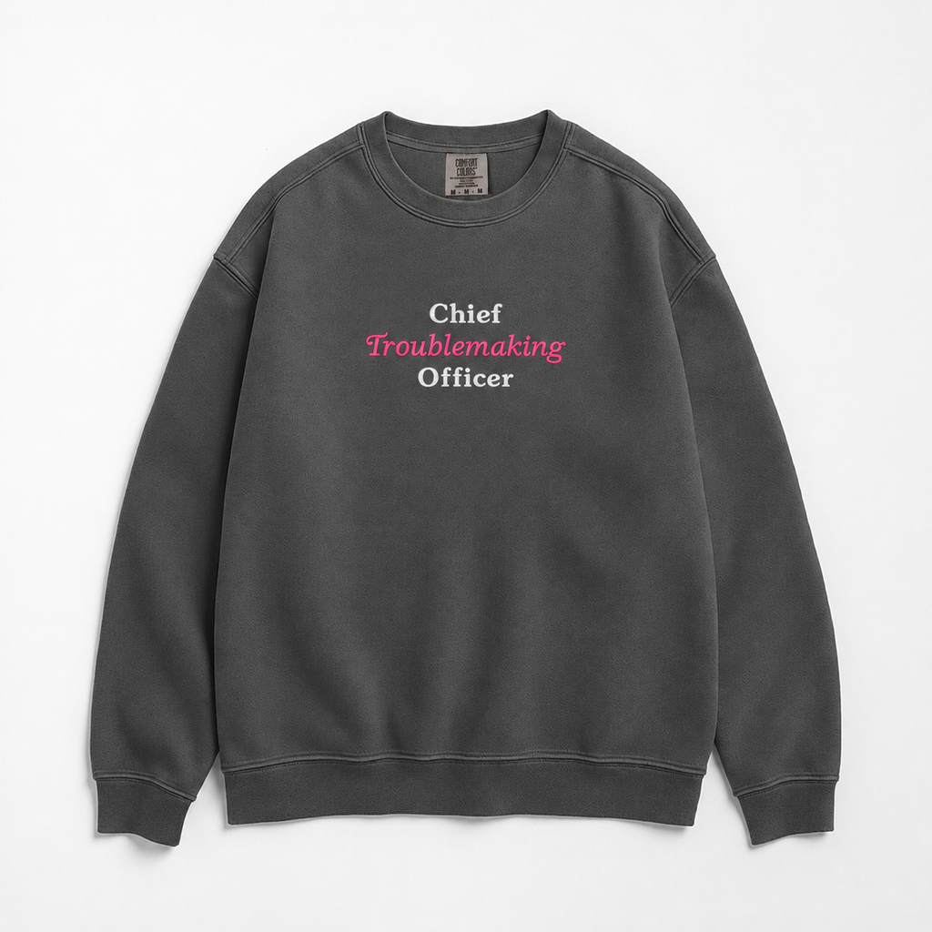 A dark gray crewneck sweatshirt with the text 'Chief Troublemaking Officer' printed on the chest in white and pink lettering, displayed flat against a light gray background.