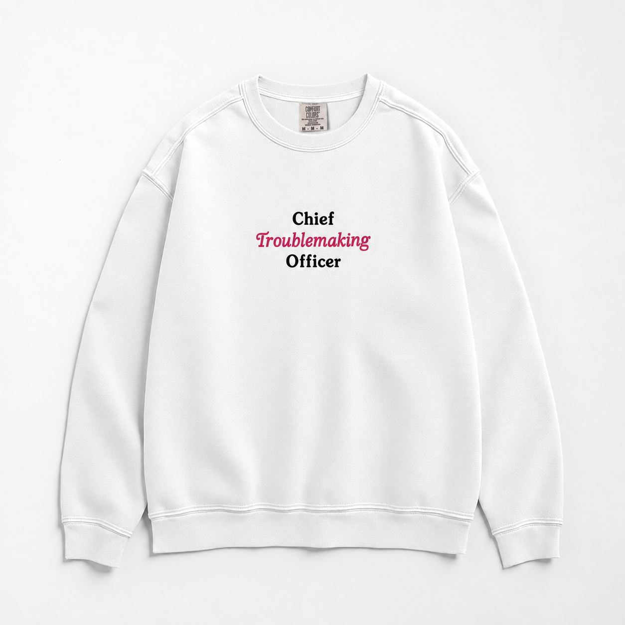 A white crewneck sweatshirt with the text 'Chief Troublemaking Officer' printed on the chest, featuring 'Chief' and 'Officer' in black and 'Troublemaking' in pink. The sweatshirt is laid flat against a clean white background.