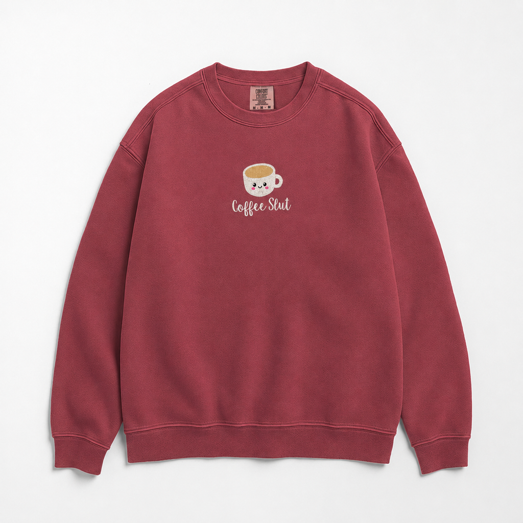 A dusty rose red crewneck sweatshirt featuring a cute embroidered cartoon coffee cup with the text 'Coffee Slut' written on the center chest, displayed against a clean white background.