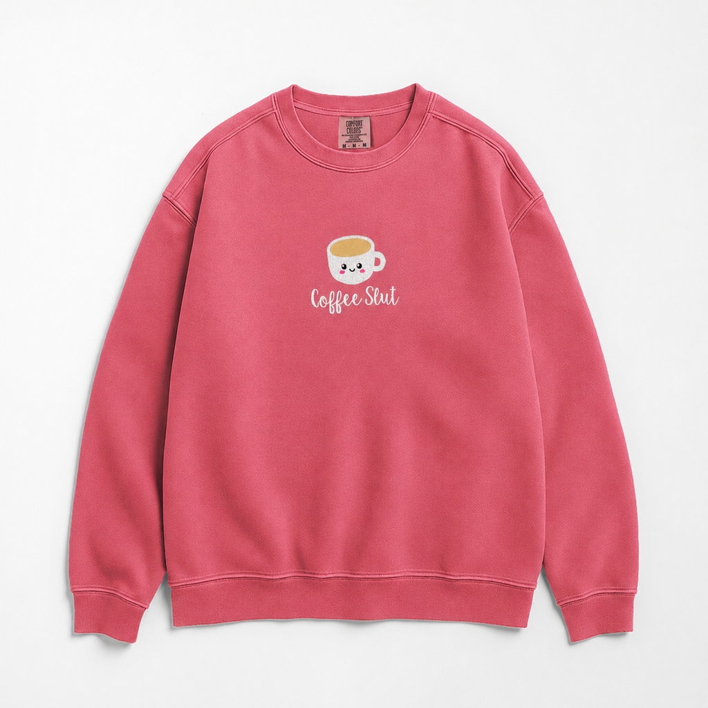A pink crewneck sweatshirt featuring an embroidered coffee cup with 'Coffee Slut' written on the chest, displayed against a clean white background.