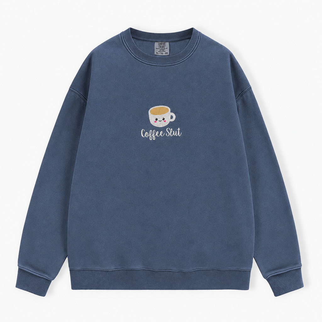 A washed blue crewneck sweatshirt featuring a cute cartoon coffee cup embroidered with a smiling face and the text 'Coffee Slut' on the chest, displayed against a clean white background.