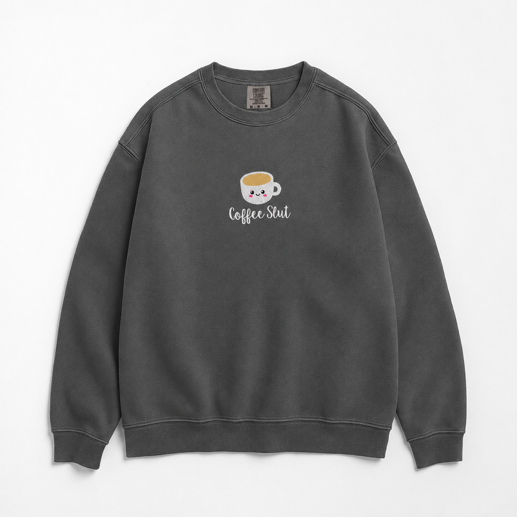 A dark gray crewneck sweatshirt featuring a cute cartoon coffee cup embroidered with a smiling face and the text 'Coffee Slut' written below it, displayed on a clean white background.