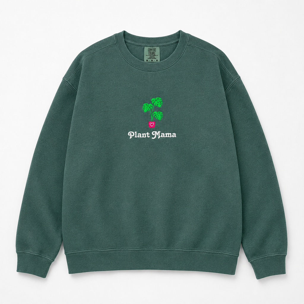 A dark green crewneck sweatshirt featuring an embroidered monstera plant with in a pink pot and the text 'Plant Mama' in white gothic font.