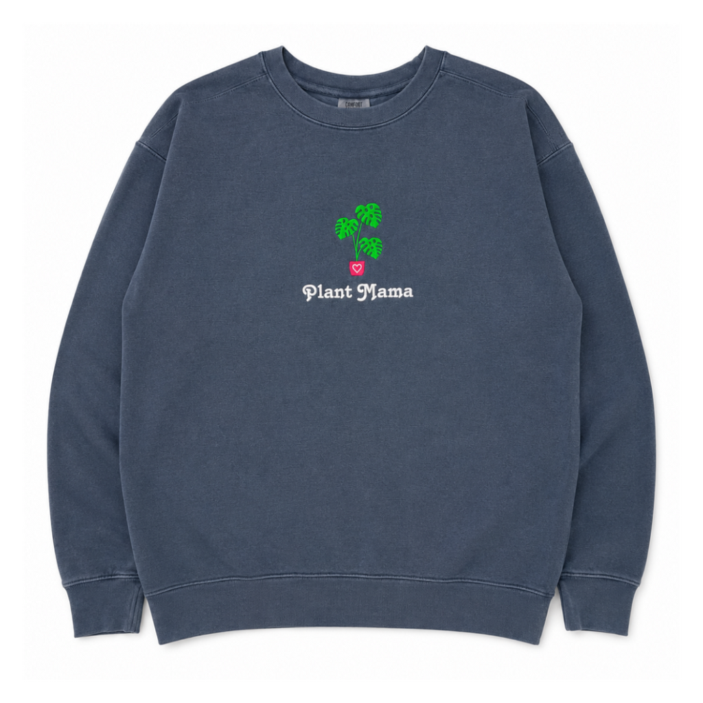 A dark slate blue crewneck sweatshirt featuring an embroidered monstera plant with in a pink pot and the text 'Plant Mama' in white gothic font.