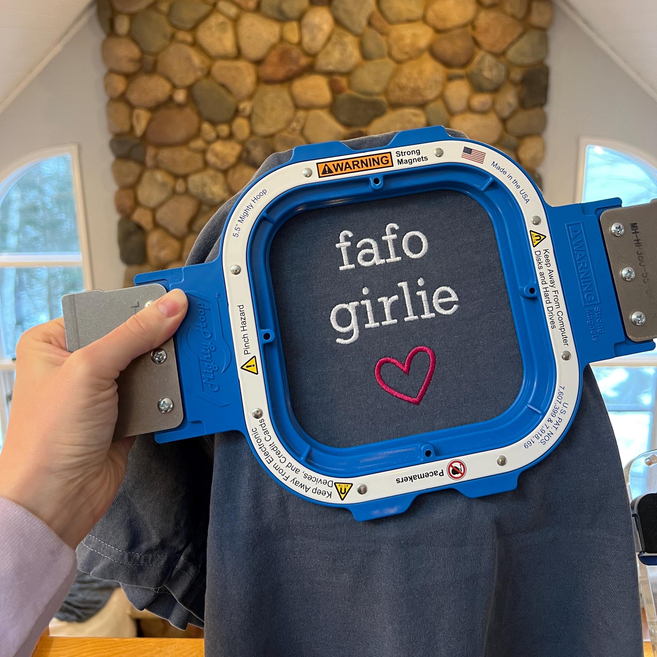 Person holding a blue embroidery machine with 'fafo girlie' text and heart design.