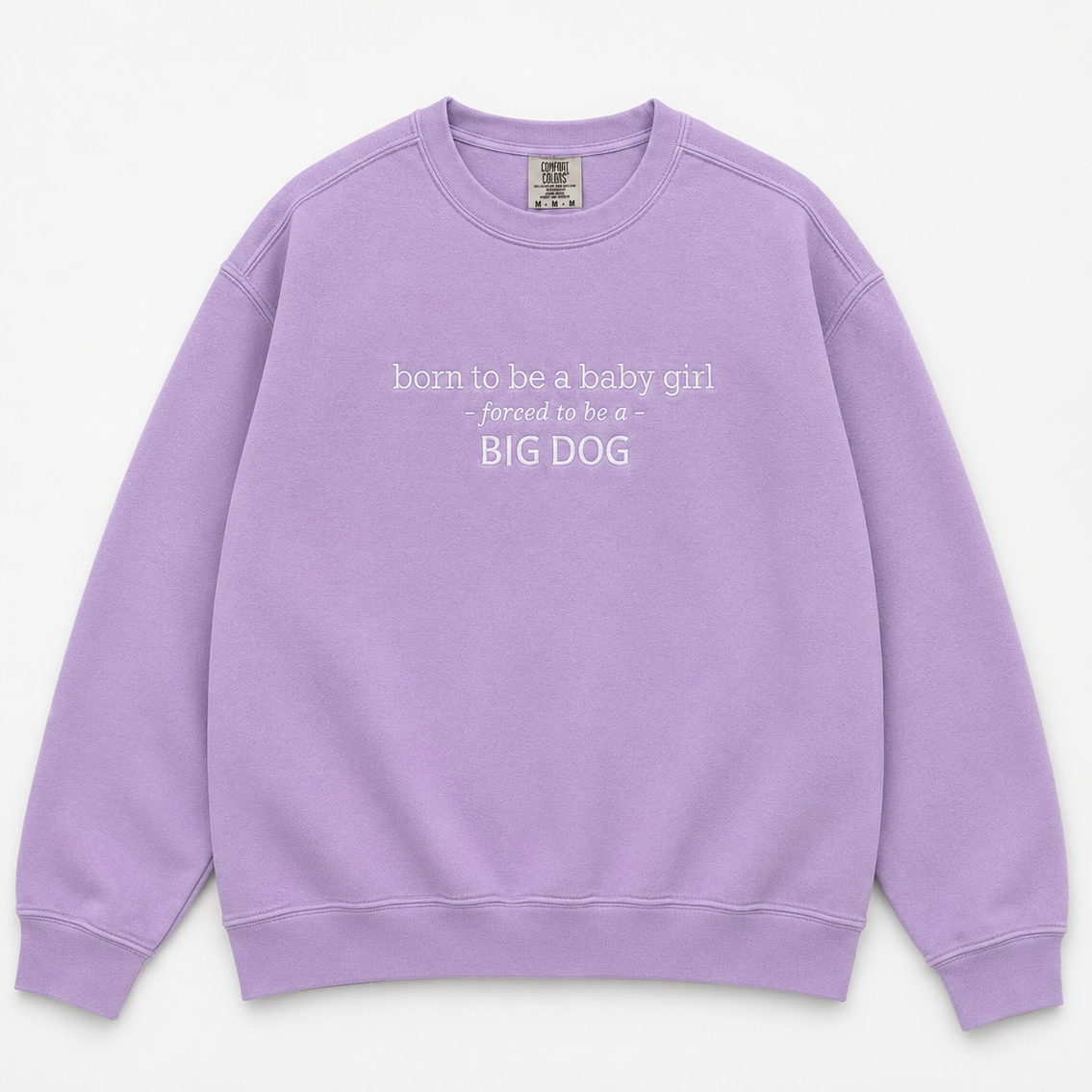 A lavender purple crewneck sweatshirt with white text on the chest reading 'born to be a baby girl forced to be a BIG DOG', displayed flat against a light off-white background.