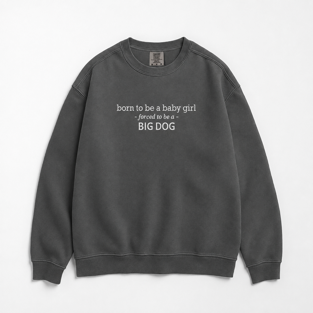 A grey crewneck sweatshirt with white text on the chest reading 'born to be a baby girl -forced to be a - BIG DOG', displayed flat against a white background.