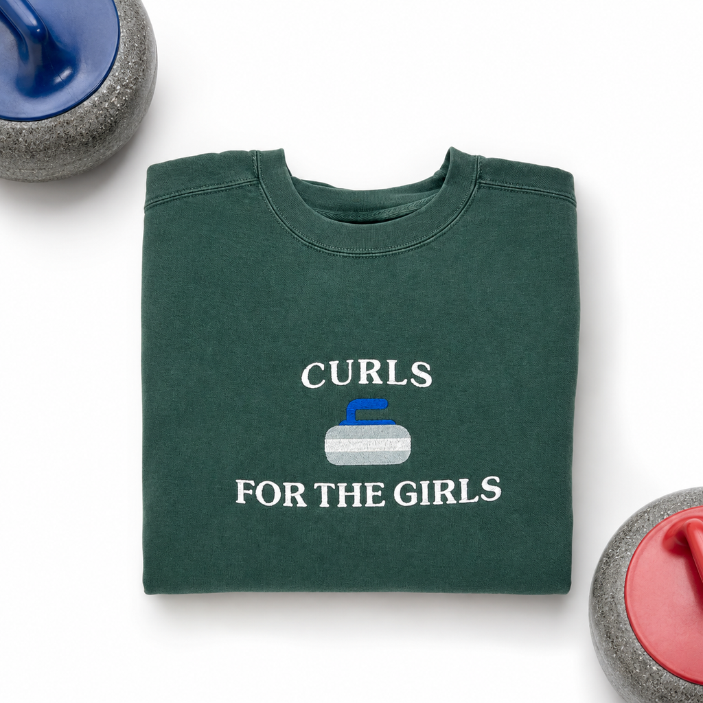 A folded dark green crewneck sweatshirt with the text 'CURLS FOR THE GIRLS' and a curling stone graphic embroidered on the front, styled on a white background with curling stones partially visible in the corners.