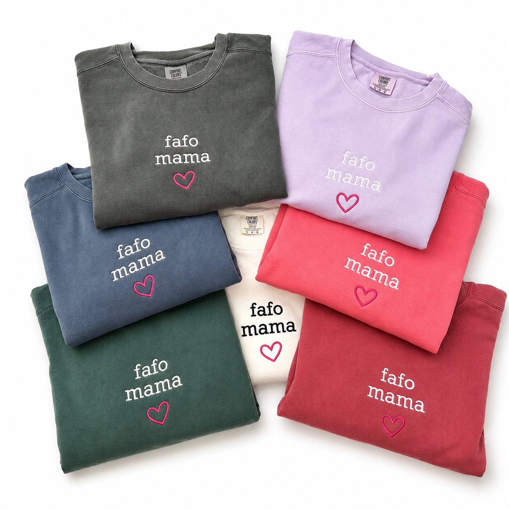 Six folded crewneck sweatshirts in different colors (gray, lavender, blue, green, white, red, pink) arranged in a fan shape on a white background. Each sweatshirt features the text 'fafo mama' in white embroidered font with a small pink heart underneath.
