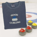 Folded blue sweatshirt with 'Good Curling' text and curling stones on a white background