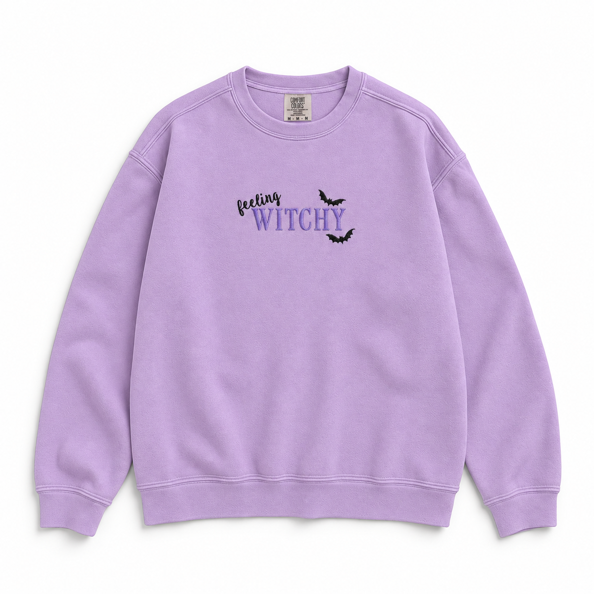 A lavender purple crewneck sweatshirt featuring the graphic text 'feeling WITCHY' in black and purple with two small black bats, displayed on a clean white background.