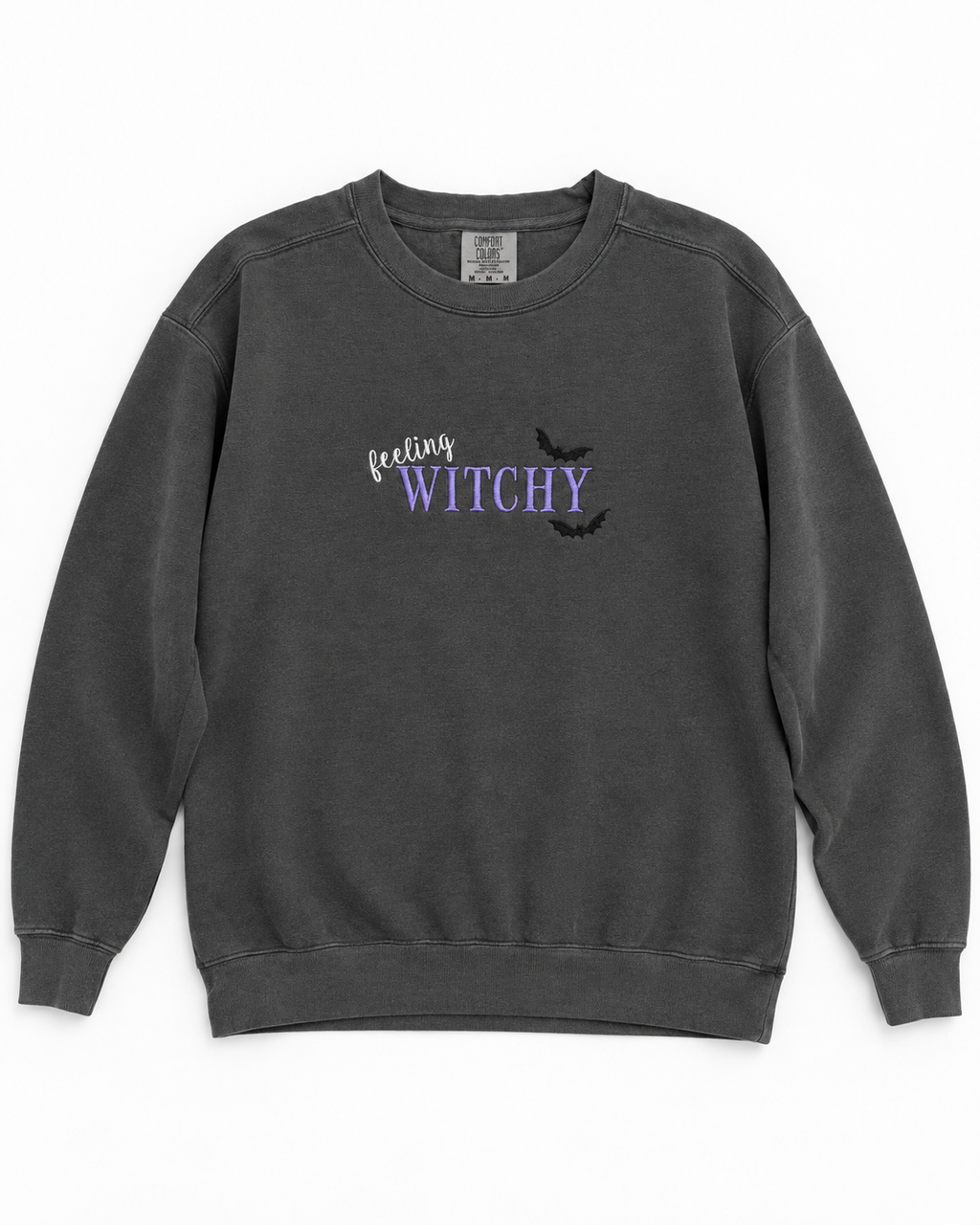 A dark gray crewneck sweatshirt featuring a 'feeling WITCHY' graphic on the chest with purple text, black bats, and a small white script word, displayed flat against a white background.