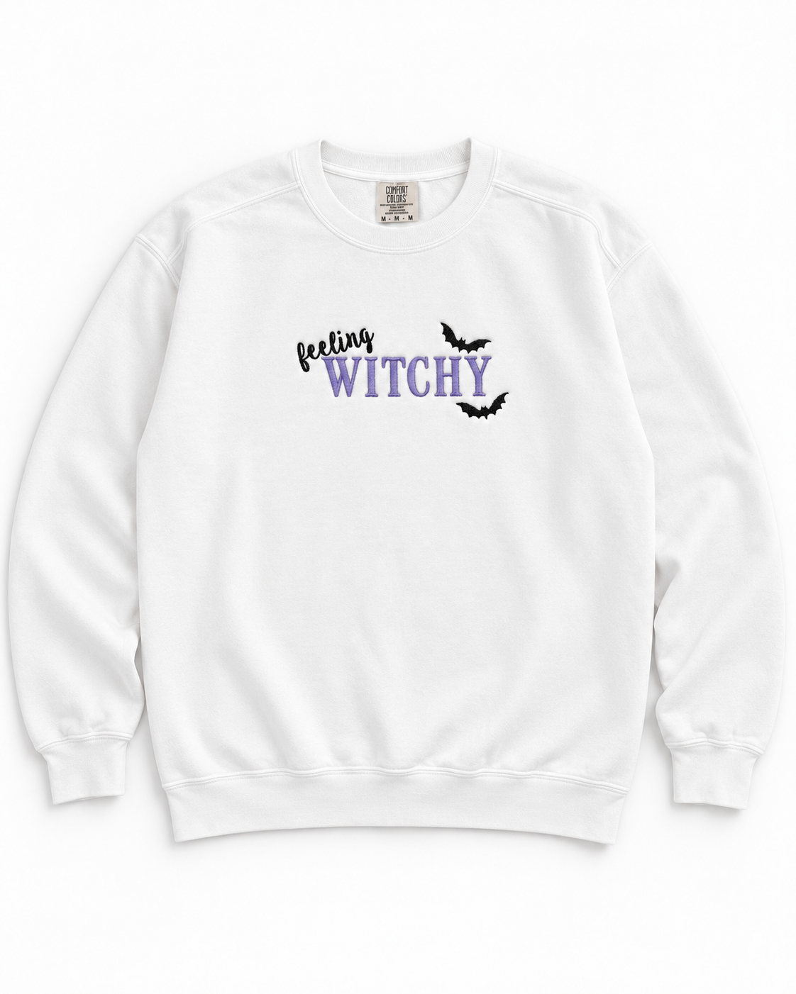 A white crewneck sweatshirt featuring a graphic on the chest that reads 'feeling WITCHY' in black and purple lettering, accented with two small black bat silhouettes, shown against a plain white background.