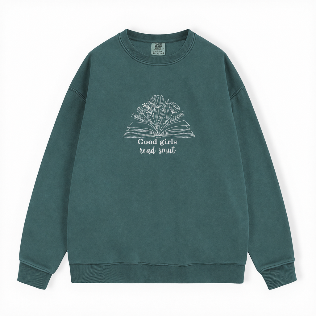 A dark green crewneck sweatshirt with a white graphic of an open book and flowers, featuring the text 'Good girls read smut' on the front, displayed against a clean white background.