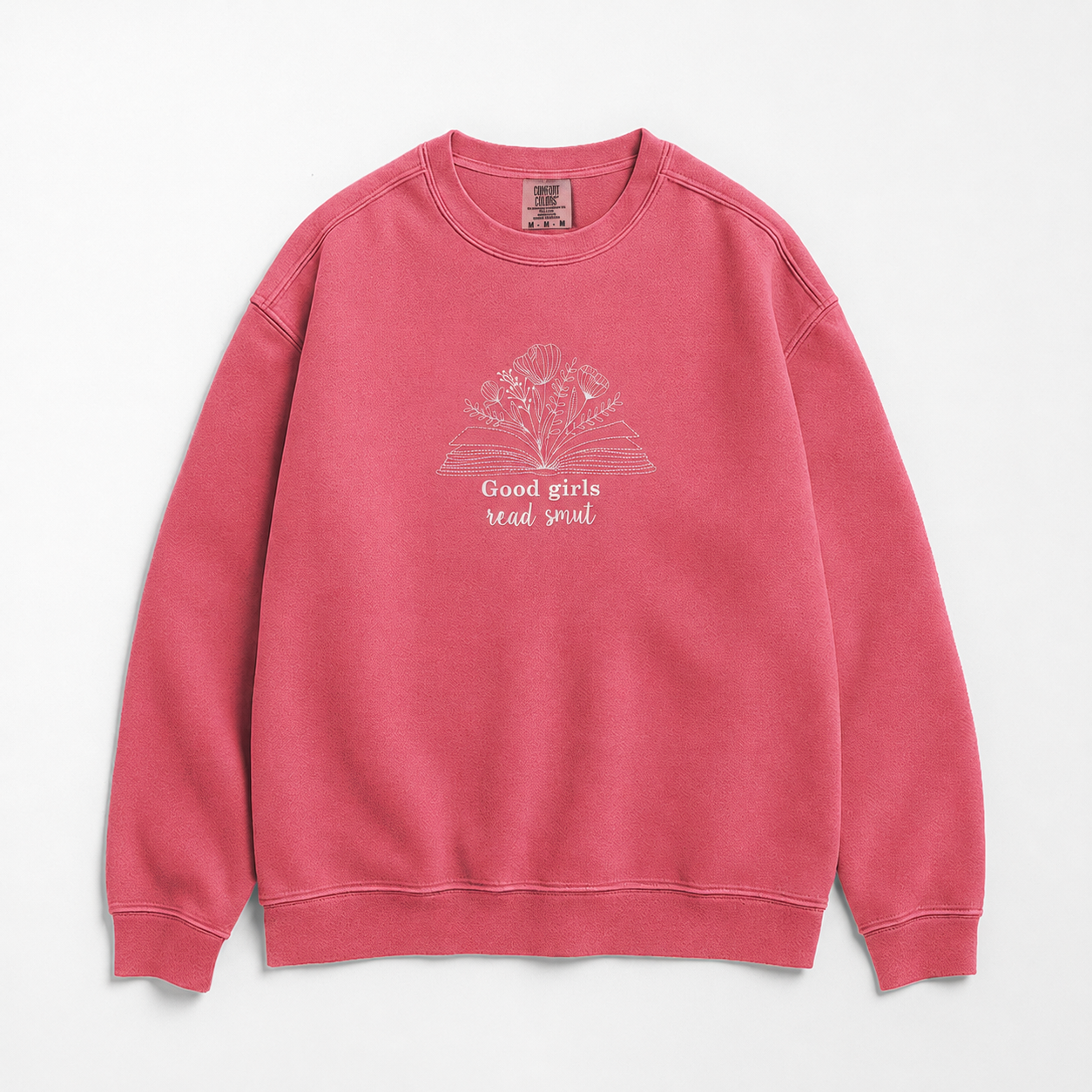A pink crewneck sweatshirt featuring a white graphic of an open book with flowers and the text 'Good girls read smut' on the front, displayed against a clean white background.