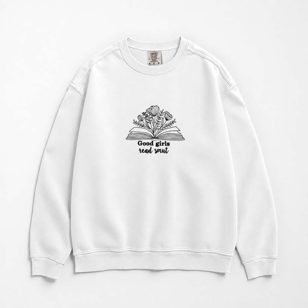 A white crewneck sweatshirt featuring a black line art graphic of an open book with flowers growing out of it and the text 'Good girls read smut' printed below, displayed on a clean white background.