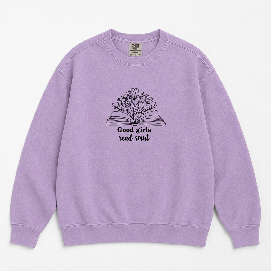 A lavender crewneck sweatshirt featuring a black line art graphic of an open book with flowers growing from it and the text 'Good girls read smut' printed on the chest, displayed against a clean off-white background.
