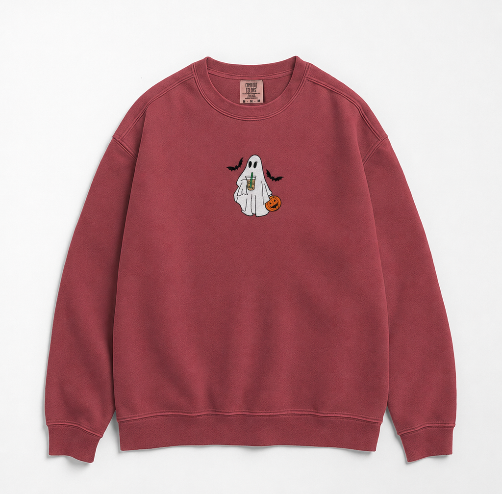 A dusty rose crewneck sweatshirt featuring a small embroidered Halloween graphic of a white ghost holding an iced coffee and a small orange pumpkin, displayed on a clean white background.