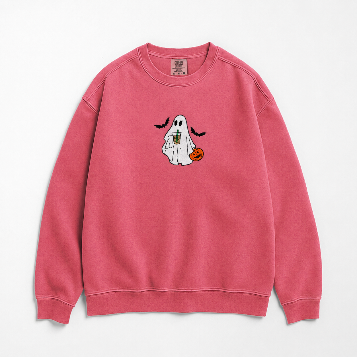 A pink crewneck sweatshirt featuring a cute cartoon ghost graphic on the chest, holding an iced coffee and a small orange pumpkin, with two black bats flying above. The sweatshirt is laid flat against a clean white background.