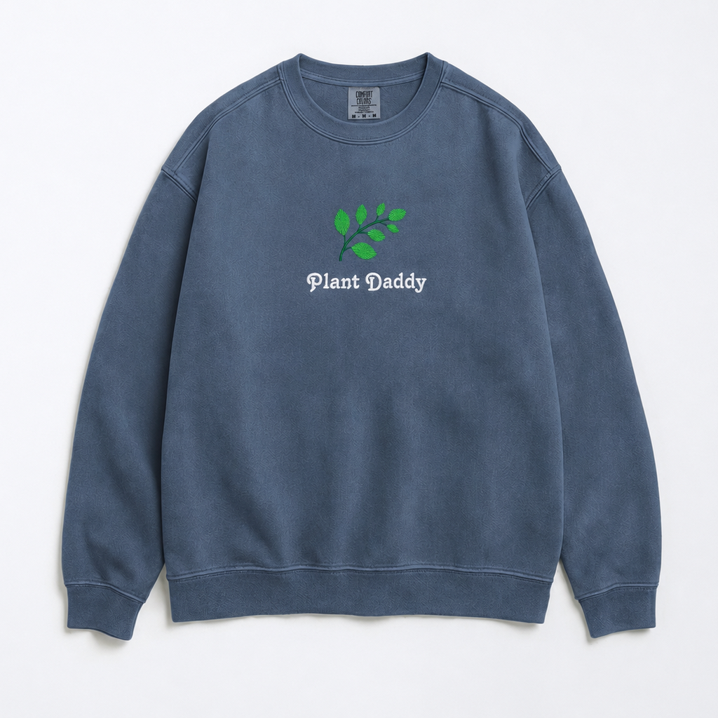 A faded blue crewneck sweatshirt featuring an embroidered green leaf graphic and the text 'Plant Daddy' on the chest, displayed flat against a clean white background.