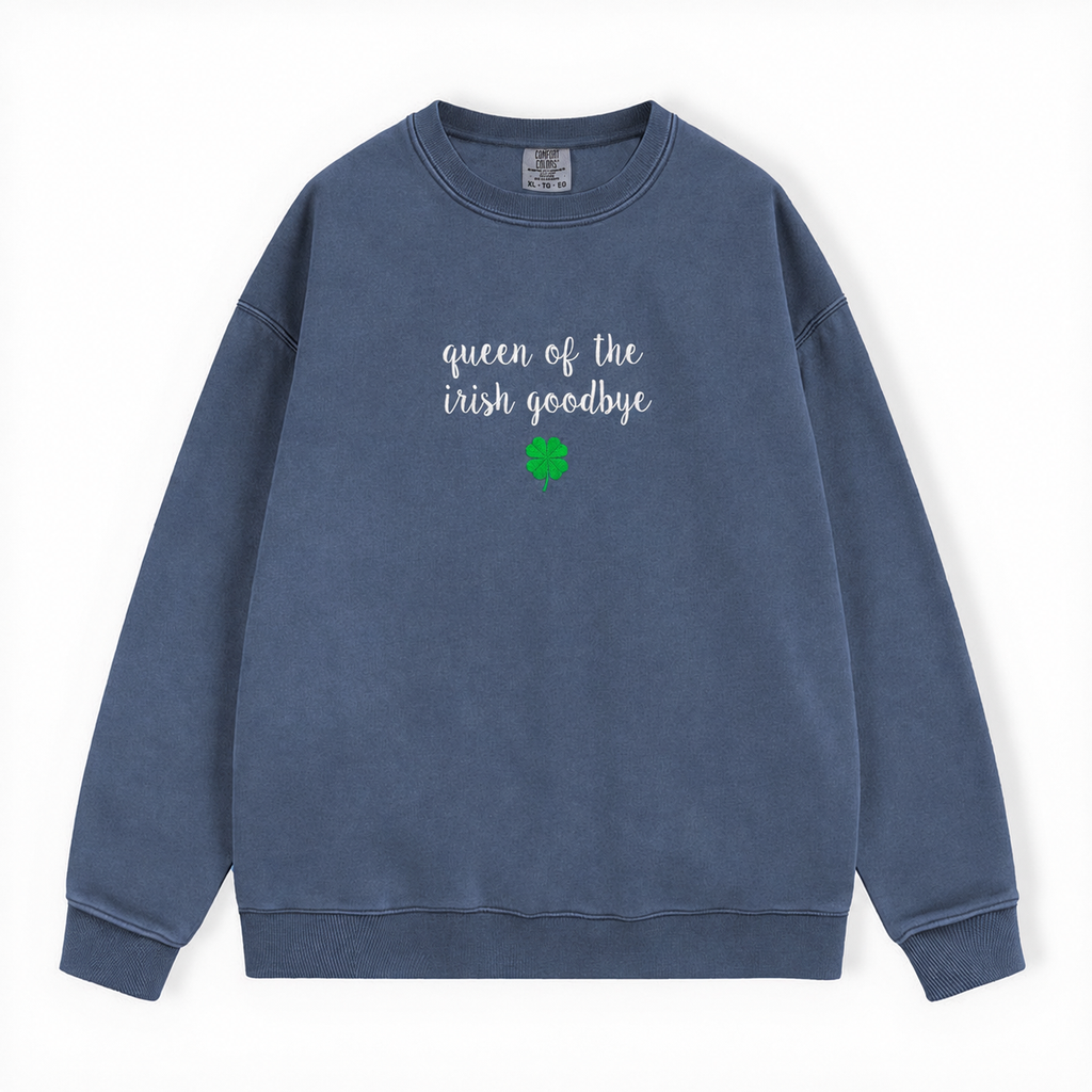 A slate blue crewneck sweatshirt with 'queen of the irish goodbye' embroidered in white script on the chest, accompanied by a small four leaf green shamrock graphic below, displayed on a clean white background.