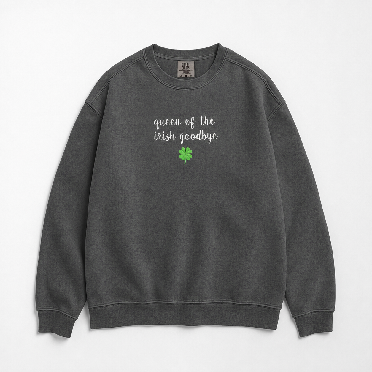 A dark gray crewneck sweatshirt featuring  embroidered text of 'queen of the irish goodbye' in white script and a small green four-leaf clover graphic on the chest, displayed flat against a light gray background.