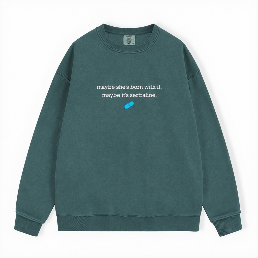 A dark green crewneck sweatshirt with white text reading 'maybe she's born with it, maybe it's sertraline.' and a small blue pill graphic on the chest, displayed flat against a white background.