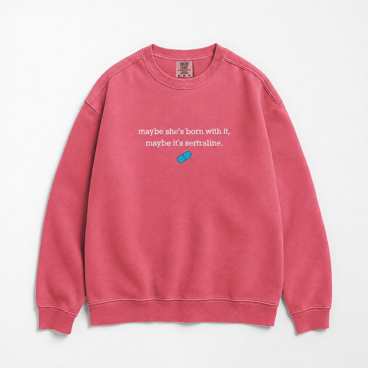 A pink crewneck sweatshirt with white text reading 'maybe she's born with it, maybe it's sertraline.' and a small blue pill graphic on the chest, displayed flat against a light gray background.