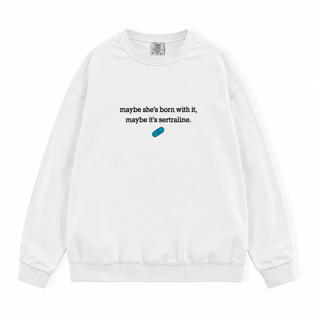A white crewneck sweatshirt with the text 'maybe she's born with it, maybe it's sertraline.' in black and a small blue pill graphic below, displayed on a clean white background.