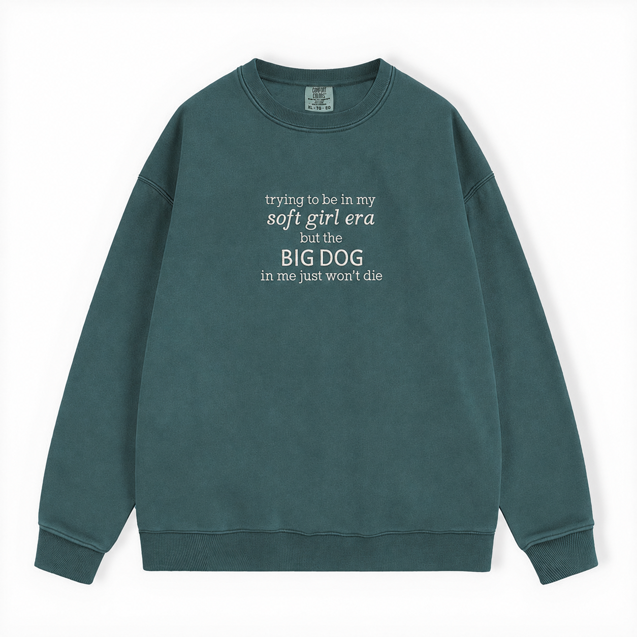 A dark green washed crewneck sweatshirt featuring the white printed text 'trying to be in my soft girl era but the BIG DOG in me just won't die', displayed on a clean white background.