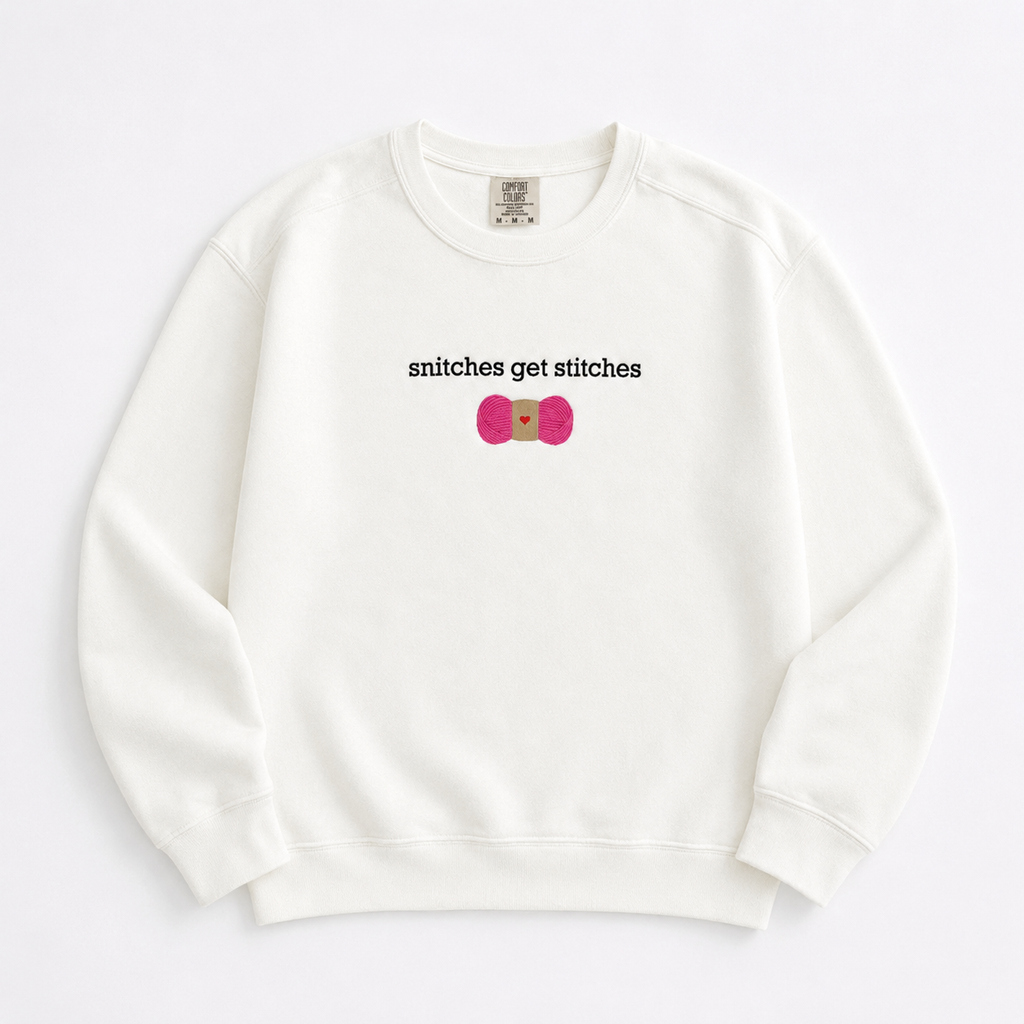 An off-white crewneck sweatshirt featuring a chest embroidered graphic with the text 'snitches get stitches' in white, below a pink skein of yarn.