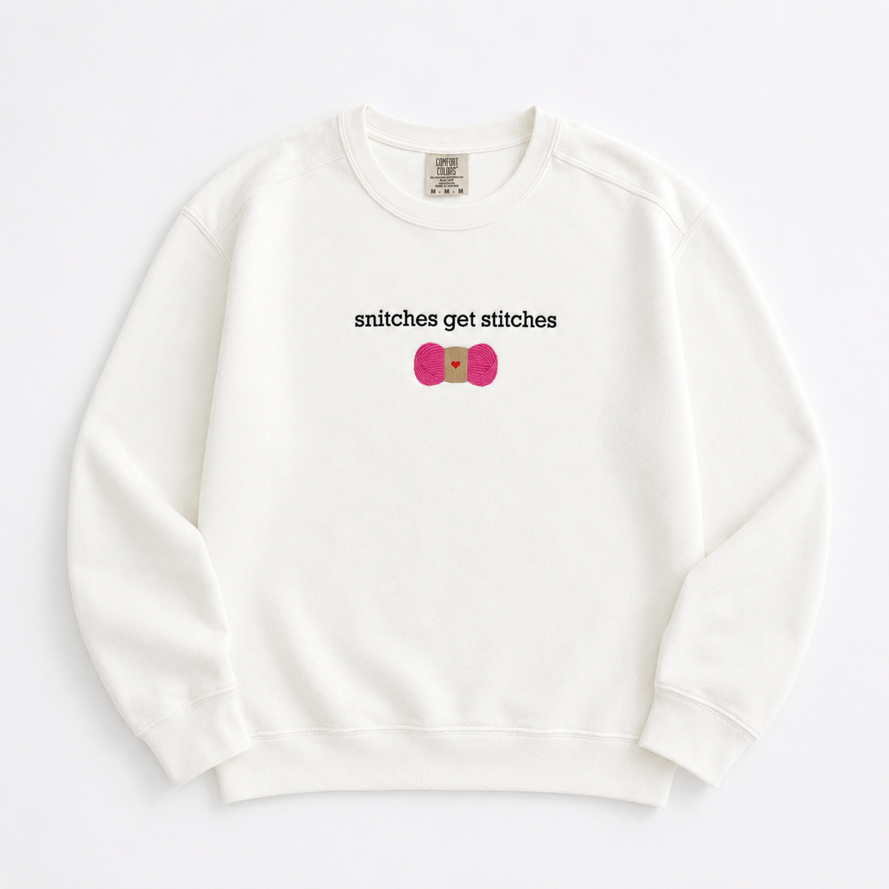 An off-white crewneck sweatshirt featuring a chest embroidered graphic with the text 'snitches get stitches' in white, below a pink skein of yarn.